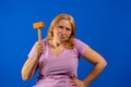 Pretty middle aged woman posing with a kitchen wooden mallet isolated on blue studio background. Royalty Free Stock Photo