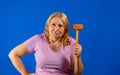 Pretty middle aged woman posing with a kitchen wooden mallet isolated on blue studio background Royalty Free Stock Photo