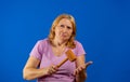 Pretty middle aged woman posing with a kitchen wooden mallet isolated on blue studio background. Royalty Free Stock Photo