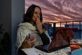 pretty middle aged woman using laptop and smart phone at same time on outdoor balcony at sunset