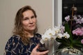 A pretty middle-aged woman 45 years old stands at the window with flowers with a glass of red holiday wine Royalty Free Stock Photo