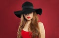 Pretty model with red lips makeup wearing black hat on red background Royalty Free Stock Photo