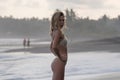 Pretty model in white bikini posing by ocean, standing in half turn to camera, Royalty Free Stock Photo