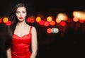 Pretty model woman in red silky dress and carnival mask on black background with abstract night glitter bokeh Royalty Free Stock Photo