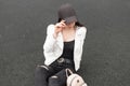 Pretty modern young woman in stylish black cap in a leather white jacket in jeans in a T-shirt with a gold backpack Royalty Free Stock Photo