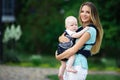 Pretty mother with baby boy in sling walking in green park Royalty Free Stock Photo