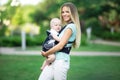 Pretty mother with baby boy in sling walking in green park Royalty Free Stock Photo