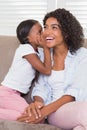 Pretty mother sitting on the couch with her daughter whispering a secret