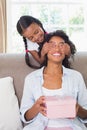 Pretty mother sitting holding gift with her daughter covering her eyes Royalty Free Stock Photo