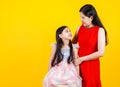 Pretty mother tenderly hug cute young daughter with love and care as sweetheart, together smile and pose to camear against yellow