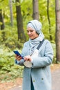 Pretty muslim woman using mobile phone outdoor. Arabic female wearing hijab using smartphone. Islamic girl texting a