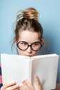 Pretty nerdy woman in spectacles reading a book against blue background