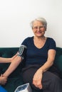 A pretty old woman, with short grey hair and her glasses on, sitting on the sofa and having her blood pressure checked