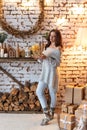 Pretty pacified young woman looking at a gift box standing near a woodpile in a retro decorated vintage New Year`s room Royalty Free Stock Photo