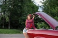 Pretty pin up girl with long curly hair checking retro car` s engine.