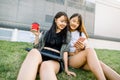 Pretty pleasant smiling Asian girlfriends spending their time together, drinking coffee while sitting on the green grass