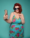 Pretty plus-size fat woman in fashion sunglasses and colorful clothes does fashion selfie like she is nice and shy girl on mint