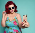Pretty plus-size fat woman in fashion sunglasses and colorful clothes does fashion sexy selfie on mint
