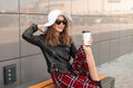 Pretty positive woman with sweet smile in vintage sunglasses in hat in casual red-black clothes sit on bench with coffee and Royalty Free Stock Photo