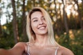 Pretty positive young blond woman with a beautiful smile with blue eyes makes a selfie in the forest on a sunny summer day. Royalty Free Stock Photo