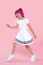 Adorable kid dancing with headphones, over pink background. Happy ittle girl dancing in studio. Full length portrait.