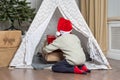 A preschooler boy in a Santa hat hides his gifts in a children& x27;s tent wigwam in the nursery. The child wants to be