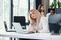 Pretty purposeful young female office manager entering datas from financial report to laptop in the modern office