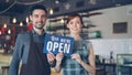 Pretty red-haired businesswoman cafe owner is holding Yes We Are Open sign with her employee in apron standing near her Royalty Free Stock Photo