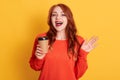 Pretty red haired female prefers coffee take away, holds disposable cup with aromatic hot drink, looking at camera with glad Royalty Free Stock Photo