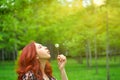 Pretty red-haired woman blows away a dandelion.