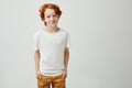 Pretty red head boy in white t-shirt looking in camera with unsatisfied expression when friend refused go to cinema with