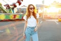 Pretty redhead beautiful young hipster woman in stylish T-shirt in vintage jeans in trendy sunglasses is walking Royalty Free Stock Photo