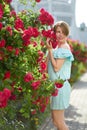 Pretty redhead girl dressed in a white light dress on a background of blooming roses. Outdoor