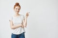 Pretty redhead girl with freckles smiling pointing finger to right. Copy space. Isolated on white. Royalty Free Stock Photo