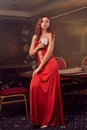 Charnimg sexy woman is posing against a poker table in luxury casino.