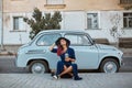 Pretty relaxing woman in hat sitting near vintage blue car. Lady with cup of drink. Leisure time, coffee break concept Royalty Free Stock Photo