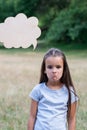 Pretty sad thinking little girl posing summer nature outdoor with cloud of thoughts like in comic book. Kid`s portrait. Emotion Royalty Free Stock Photo