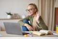 Pretty school girl waving at laptop screen at home