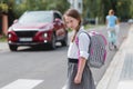 Schoolgirl with pigtails and a pink - gray backpack is standing on one-way street