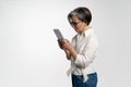 Pretty senior woman using tablet computer at office in white shirt and denim pants. The use of technology by the elderly Royalty Free Stock Photo