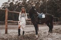 Pretty and sensual young woman wearing the dress is holding the reins and posing with the horse on the ranch Royalty Free Stock Photo