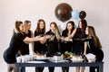 Pretty seven girls in black dresses touching the martini glasses with each other, celebrating birthday, standing near Royalty Free Stock Photo