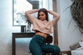 Pretty slim stylish young woman in a fashionable pink sweatshirt in trendy jeans is posing in a cozy bedroom. Attractive girl Royalty Free Stock Photo