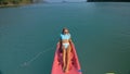 Pretty slim woman in elegant swimsuit lies in pink plastic kayak drifting on azure ocean at exotic resort upper view.