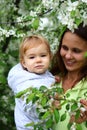 Pretty small baby girl with beautiful and smiling mother. Happy funny family in blooming garden with apple trees Royalty Free Stock Photo