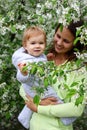 Pretty small baby girl with beautiful and smiling mother. Happy funny family in blooming garden with apple trees Royalty Free Stock Photo