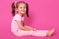 Pretty small kid with two pony tails and many colourful scrunchies sits on floor and glad to be photographed in photo studio. Royalty Free Stock Photo