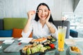 Pretty smiling Asian girl sitting at the table and holding sushi roll in front of eye. Beautiful young woman eating Royalty Free Stock Photo