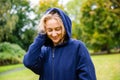 Pretty smiling blond female wearing long hoodie with hood on her head looking down, outdoor in the city park in autumn season Royalty Free Stock Photo
