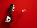 Pretty smiling brunette woman in tight red dress with soccer ball in her hand looks up dreamly and counts her fingers